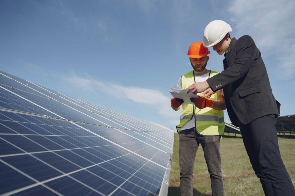 Electrical employee and contractor looking at paperwork next to a solar panel
